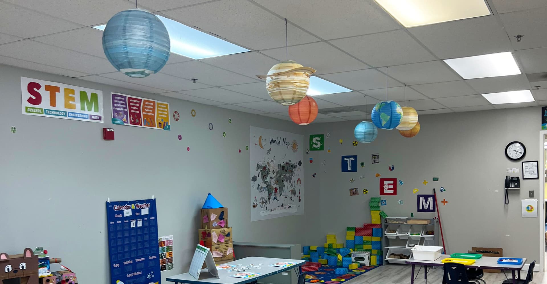 A STEM classroom with hanging planet lanterns, a world map, foam building blocks and a STEM wall display